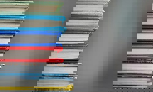 Six books piled one of top of the other, showing coloured edges of spines and covers against a grey background
